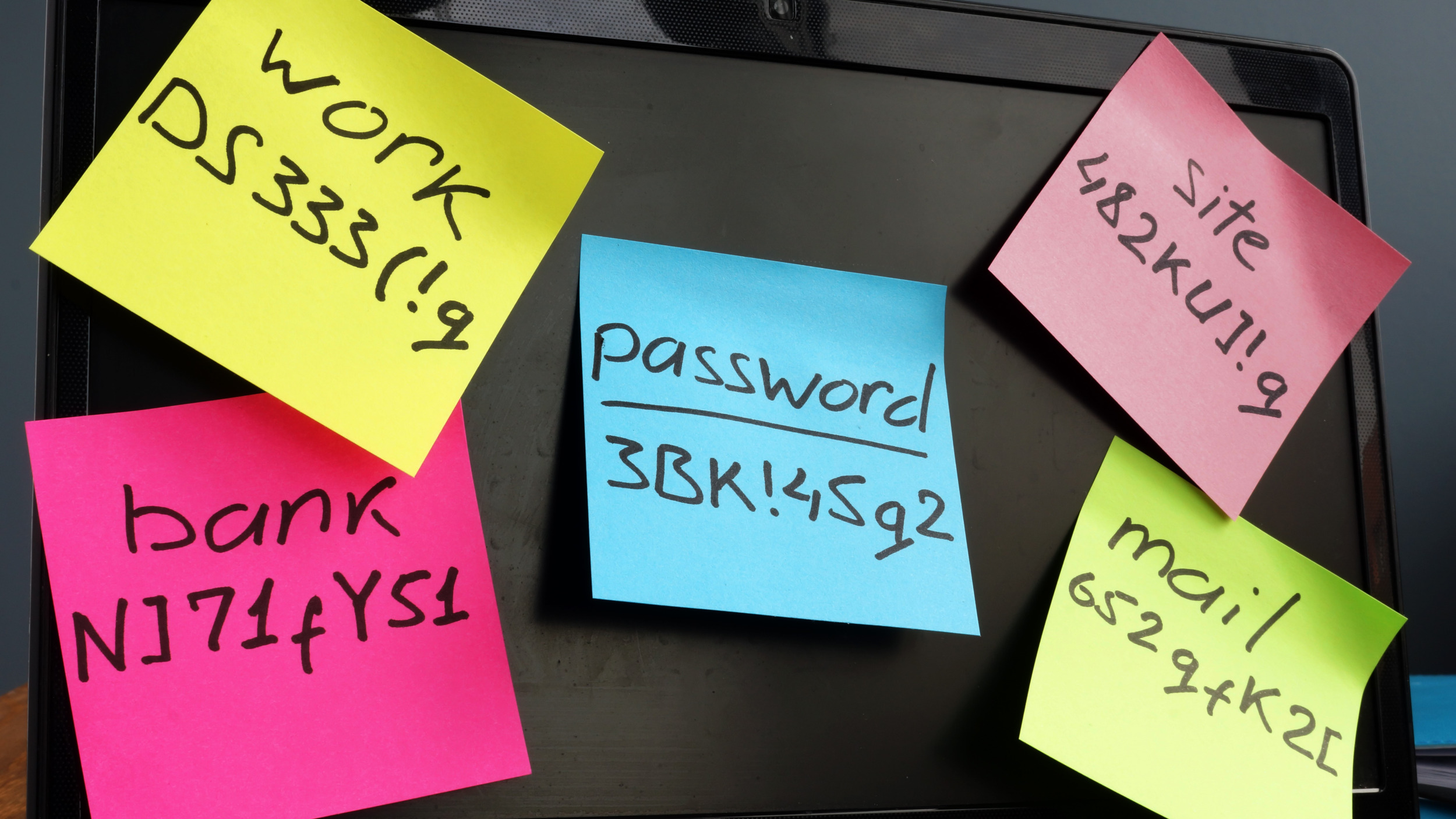 Computer covered in sticky notes showing passwords for bank, accounts and devices, highlighting weak password security and cybersecurity vulnerabilities.